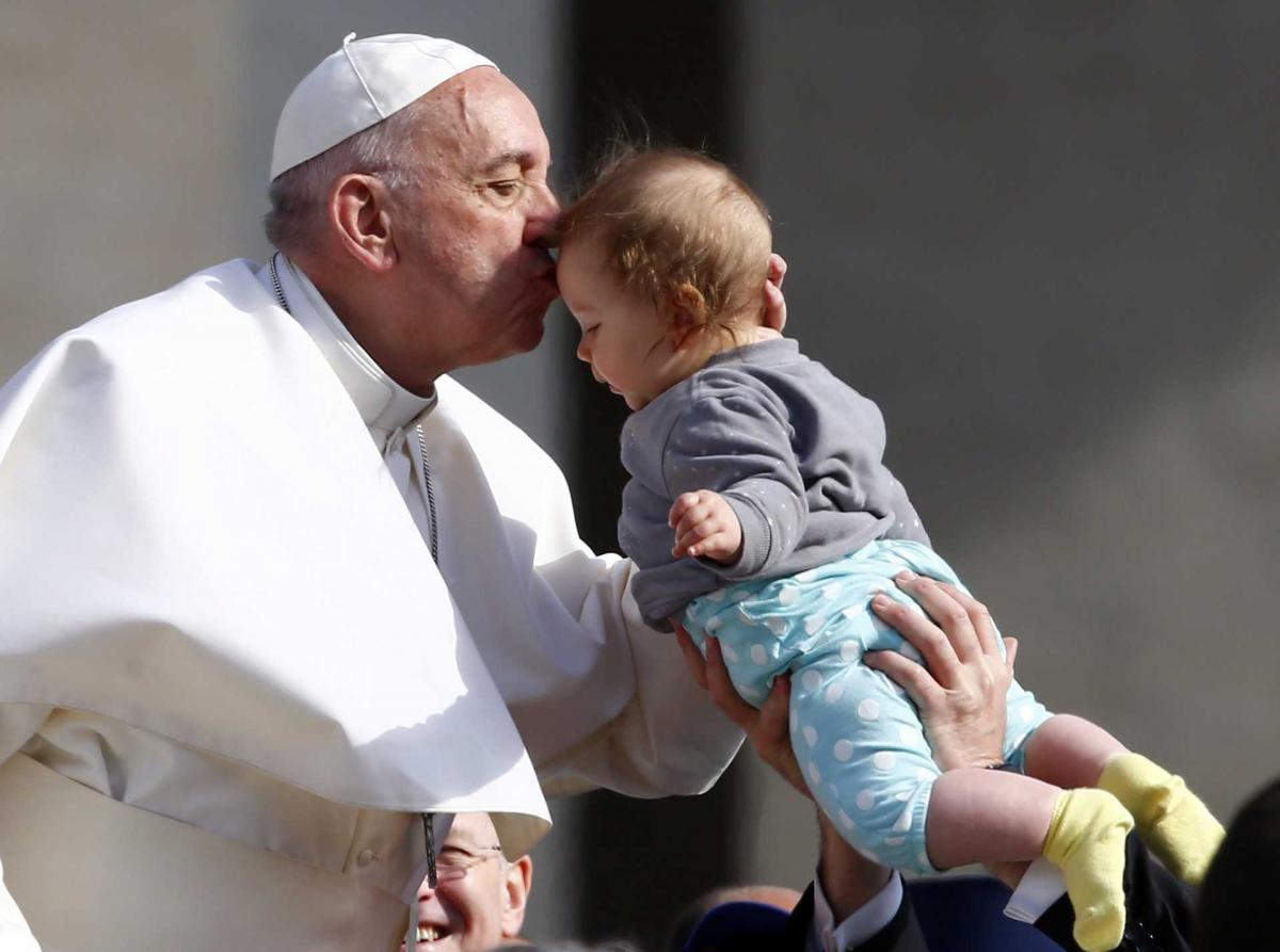 Pope Francis kisses a child as he arrives to lead his Wednesday general audience in Saint Peter’s square at the Vatican